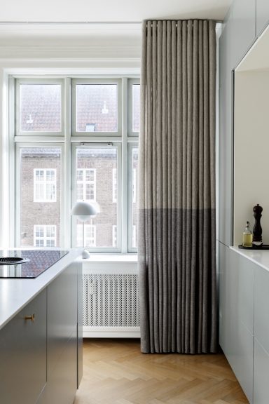 Modern kök med stora fönster, snyggt husgeråd och gardiner med vertikala ränder.